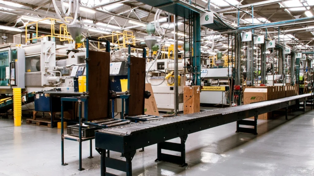 Long factory assembly line with metal machinery, a rolling conveyor, and numbered stations (6–12) under bright overhead lighting.