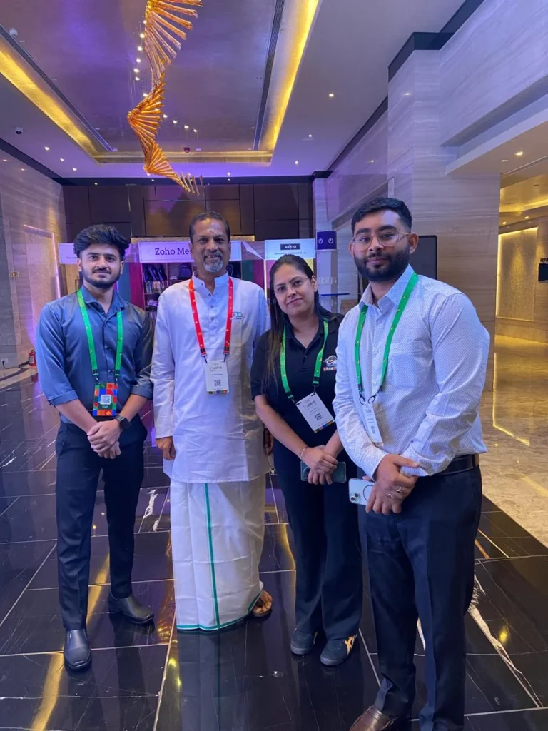 Four professionals posing for a photo in a modern lobby, all wearing conference badges and lanyards.